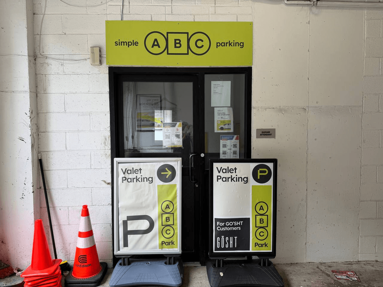 The valet attendant office just inside the garage, with a lime simple ABC parking sign and two Valet Parking boards.