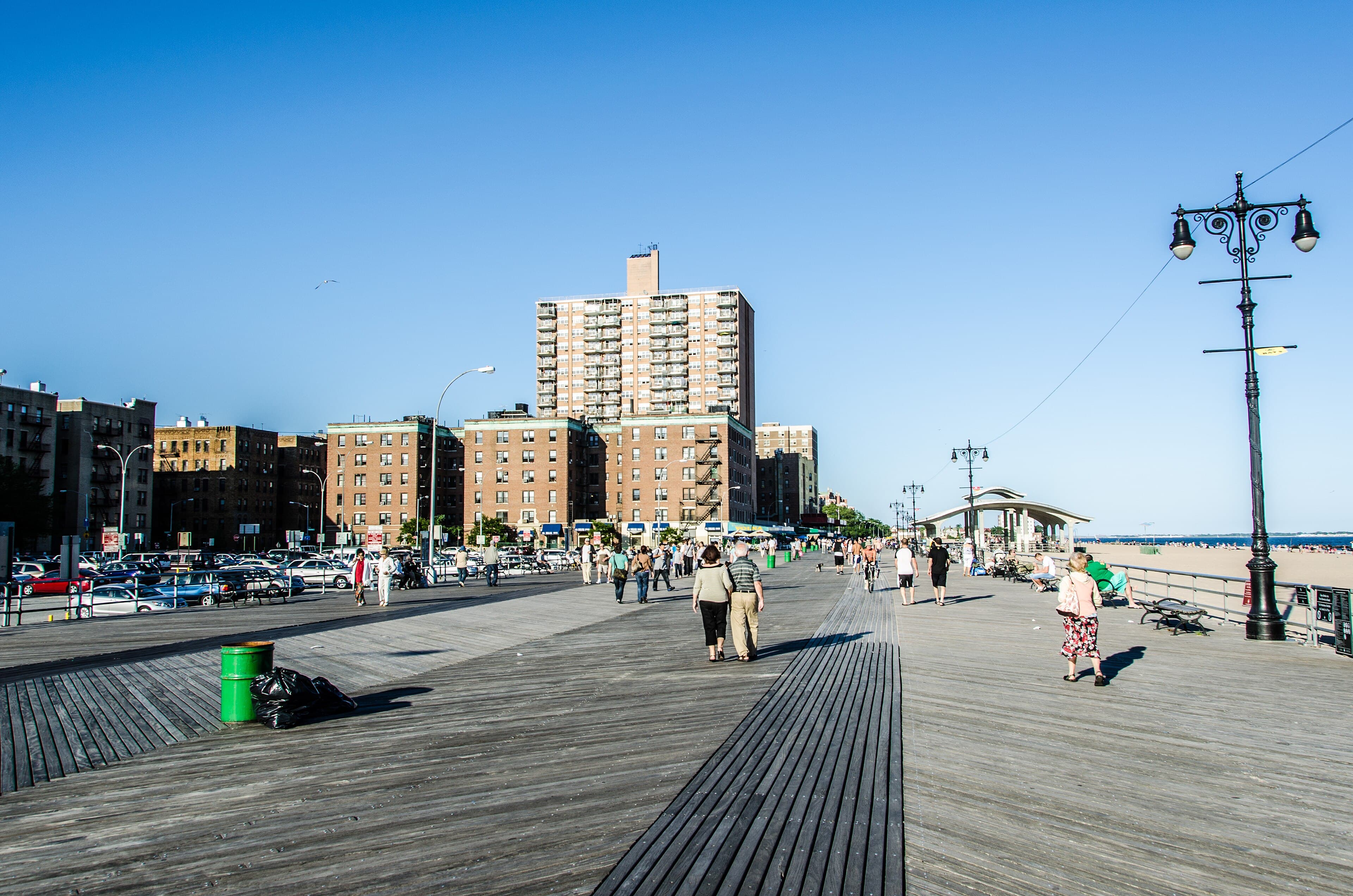 A sunny view along Brighton Beach's boardwalk in Brooklyn, with seafront buildings, lamps and the ocean.